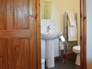 Ein Badezimmer mit Holztür, weißem Waschbecken, Spiegel, Handtuchhalter und Toilette.
