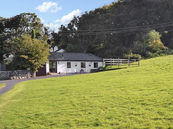A white cottage with a stone wall, a wooden fence, and a grassy hill.