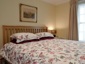 A bedroom with a wooden headboard, floral bedding, a nightstand with a lamp, and a framed picture on the wall. - The Old Rectory Lodge (Yaxham, near Dereham)