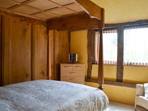 A bedroom with a wooden bed frame, a wooden dresser, and a wicker chair.