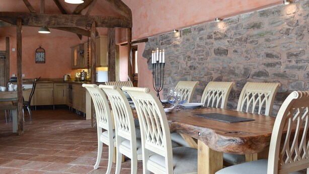 A rustic dining area with a large wooden table surrounded by white chairs, a stone wall, and exposed wooden beams. - 2 bedroom accommodation in Knapton Green, near Leominster (Knapton Green, near Leominster)