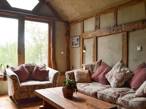 A cozy living room with a wooden bench, two patterned sofas, a potted plant, and a large window with a view of trees.
