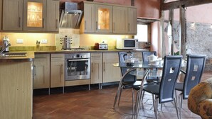 A rustic kitchen with wooden cabinets, a gas stove, a microwave, and a dining area with chairs and a table. - 2 bedroom accommodation in Knapton Green, near Leominster (Knapton Green, near Leominster)