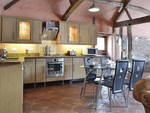 A rustic kitchen with wooden cabinets, a gas stove, a microwave, and a dining area with chairs and a table.