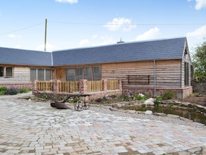 A log cabin-style building with a sloped roof, a wooden fence, and a small pond. - 2 bedroom accommodation in Knapton Green, near Leominster (Knapton Green, near Leominster)