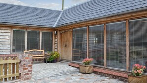 A building with a sloped roof, large windows, and a brick patio. - 2 bedroom accommodation in Knapton Green, near Leominster (Knapton Green, near Leominster)