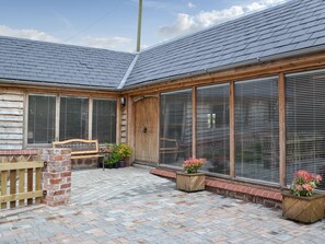 A building with a sloped roof, large windows, and a brick patio.