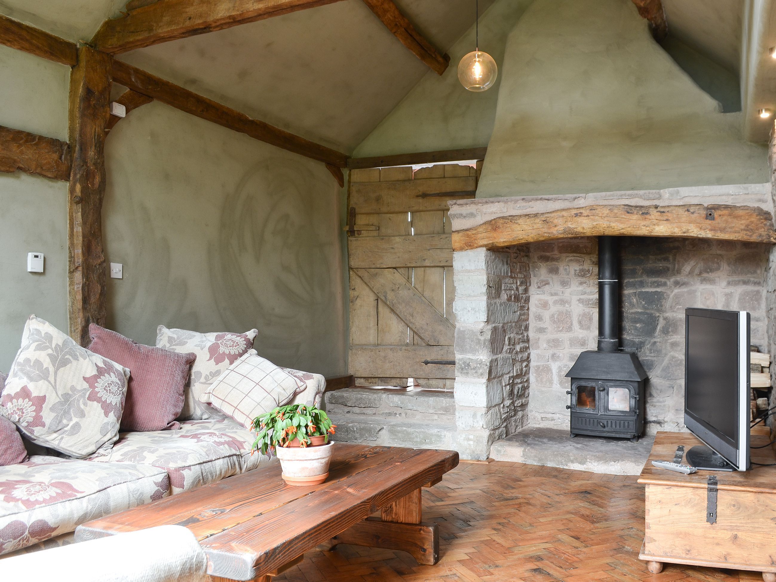 A cozy room with a stone fireplace, a wooden bench, a sofa with patterned cushions, and a television on a wooden stand.