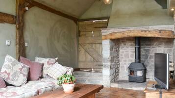 A cozy room with a stone fireplace, a wooden bench, a sofa with patterned cushions, and a television on a wooden stand.