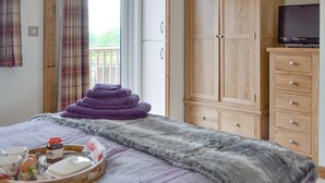 Un dormitorio con cama, un armario de madera, un televisor sobre un mueble bajo y una ventana con cortinas.