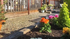Una cabaña de madera con porche cubierto, un camino de grava y plantas en macetas.