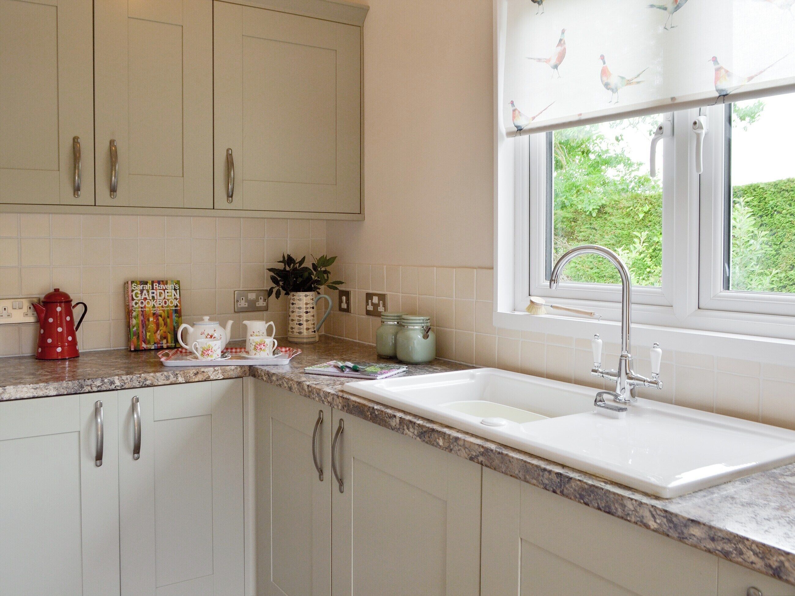 A kitchen with white cabinets, a granite countertop, a window with a view of greenery, and a sink with a faucet.
