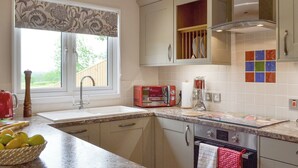 Una cocina con ventana, un tostador rojo, un lavamanos y una estufa.
