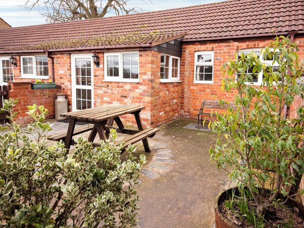 A brick building with a tiled roof, a wooden bench, and a potted plant.
