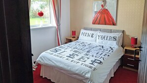 Une chambre à coucher avec un lit, une table de chevet, une lampe, une fenêtre avec des rideaux et un tableau au mur.