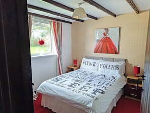 A bedroom with a bed, a nightstand, a lamp, a window with curtains, and a painting on the wall. - 3 bedroom accommodation in Woodacott, near Holsworthy (Woodacott, near Holsworthy)