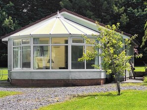 A conservatory with a brick base and white glass panels, surrounded by a gravel path and green grass. - 3 bedroom accommodation in Woodacott, near Holsworthy (Woodacott, near Holsworthy)