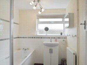 Een badkamer met een bad, een wastafel, een spiegel en een raam.