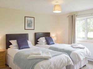Hotelkamer met twee bedden, elk met hoofdeinde, wit beddengoed en een blauwe plaid. Er hangt een ingelijste foto aan de muur en er is een raam met gordijnen.
