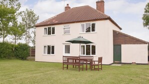 A two-story house with a tiled roof, a green door, and a patio with a wooden table and chairs. - 3 bedroom accommodation in Frostenden, near Beccles (Frostenden, near Beccles)