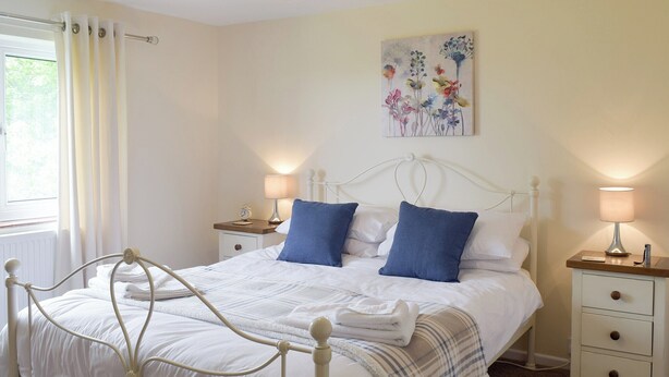 A neatly arranged bedroom with a bed, two bedside tables, a wall clock, and a floral artwork. - 3 bedroom accommodation in Frostenden, near Beccles (Frostenden, near Beccles)