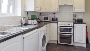 A compact kitchen with white cabinets, a washing machine, a microwave, and an oven. - 3 bedroom accommodation in Frostenden, near Beccles (Frostenden, near Beccles)