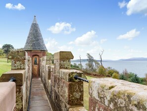 A stone pathway leading to a small building with a conical roof, overlooking a body of water and distant hills.