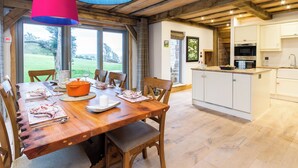 A dining area with a wooden table, chairs, and a large window overlooking a garden. - 4 bedroom accommodation in Largs (Largs)