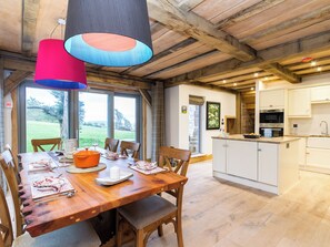 A dining area with a wooden table, chairs, and a large window overlooking a garden. - 4 bedroom accommodation in Largs (Largs)