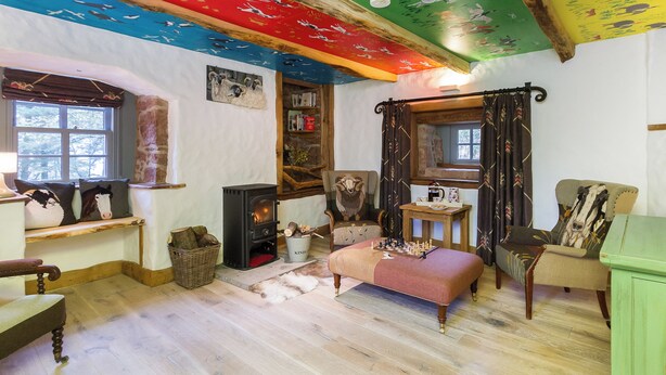 A cozy room with a fireplace, a sofa, a wooden floor, and a colorful ceiling. - 4 bedroom accommodation in Largs (Largs)