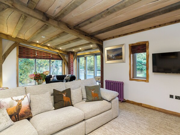 A cozy living room with a sofa, a fireplace, a television, and large windows offering a view of the outdoors.