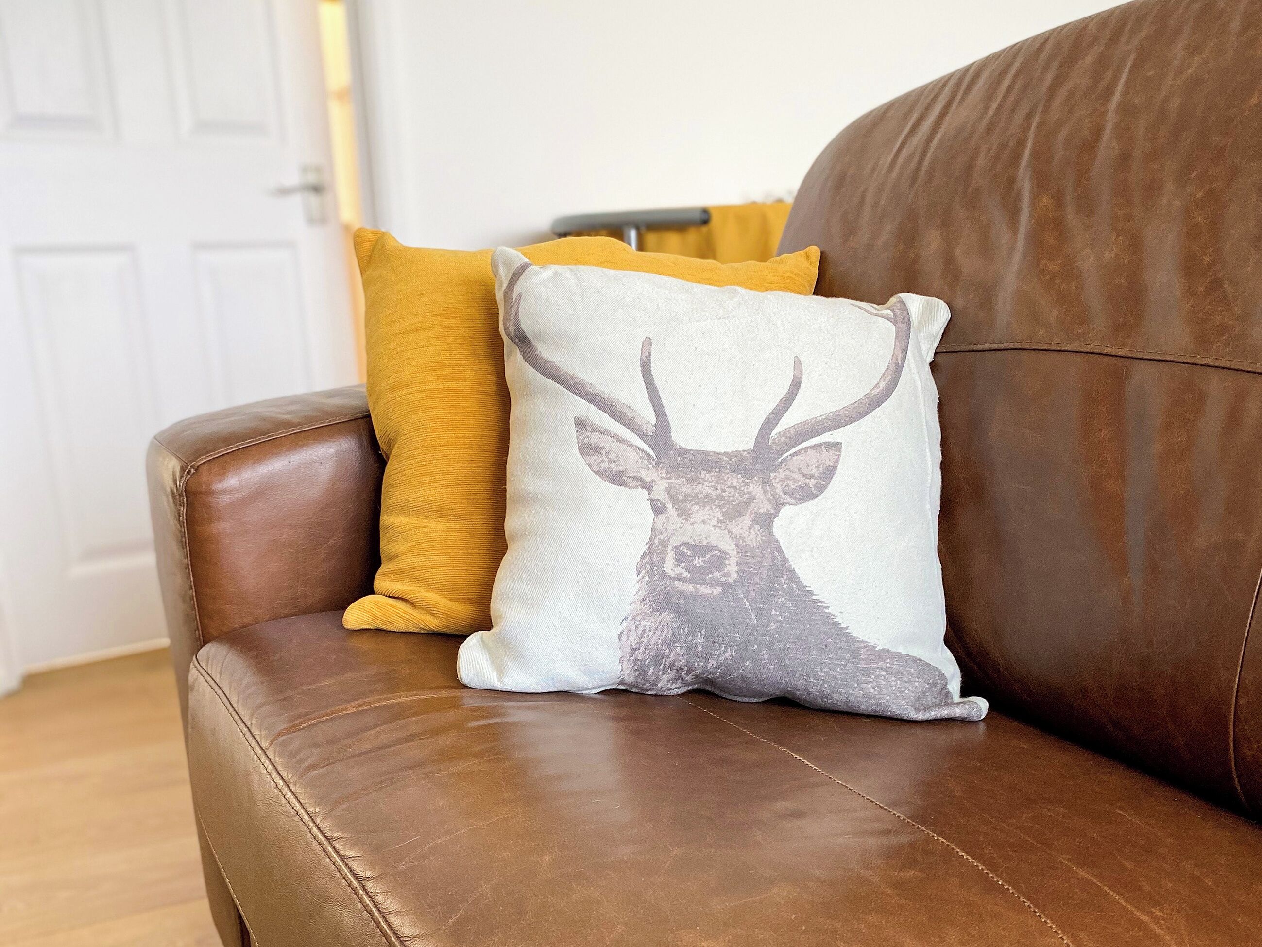 Un sofá de cuero marrón con dos almohadones decorativos, uno con estampado de ciervo y otro en color mostaza.