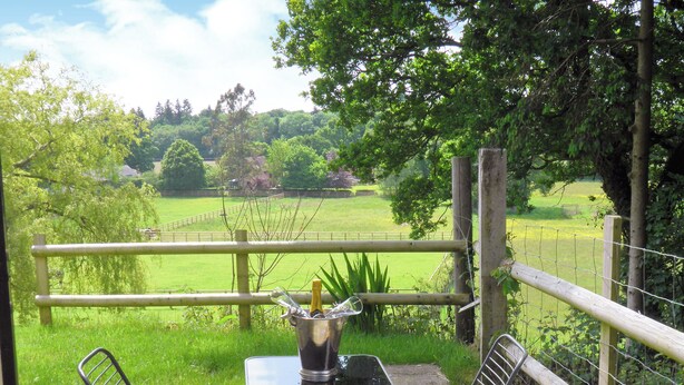 Eine Terrasse mit Tisch und zwei Stühlen, mit Blick auf ein Grasfeld und einen Holzzaun.