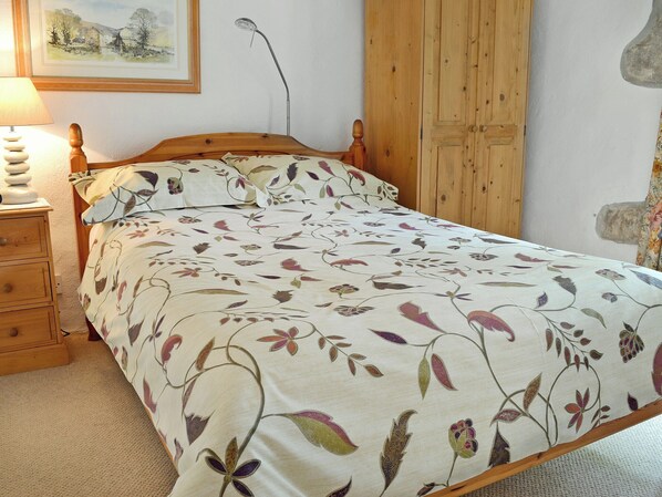 A bedroom with a wooden bed frame, a floral-patterned bedspread, a bedside table with a lamp, and a wardrobe. - Take a break with a special someone to this truly rural setting. (Breage, near Helston)