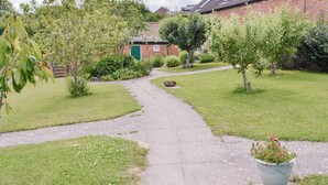 A pathway leading to a brick building with a green door, surrounded by well-maintained grass and trees. - The perfect hideaway for two. (Salwayash, near Bridport)
