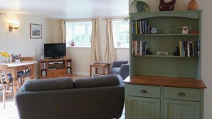 A living room with a grey sofa, a wooden coffee table, a television, a bookshelf, and a window with curtains. - The perfect hideaway for two. (Salwayash, near Bridport)