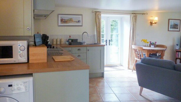 A compact kitchen with a microwave, toaster, and washing machine. There's a dining area with a table and chairs, and a sofa. - The perfect hideaway for two. (Salwayash, near Bridport)