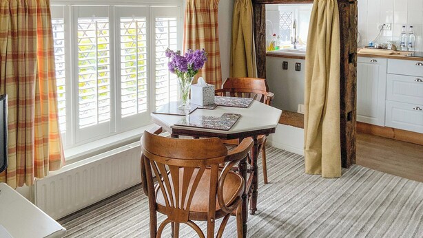A dining area with a table set for four, surrounded by wooden chairs. A vase with purple flowers is on the table. - 1 bedroom accommodation in Betley, near Nantwich (Betley, near Nantwich)