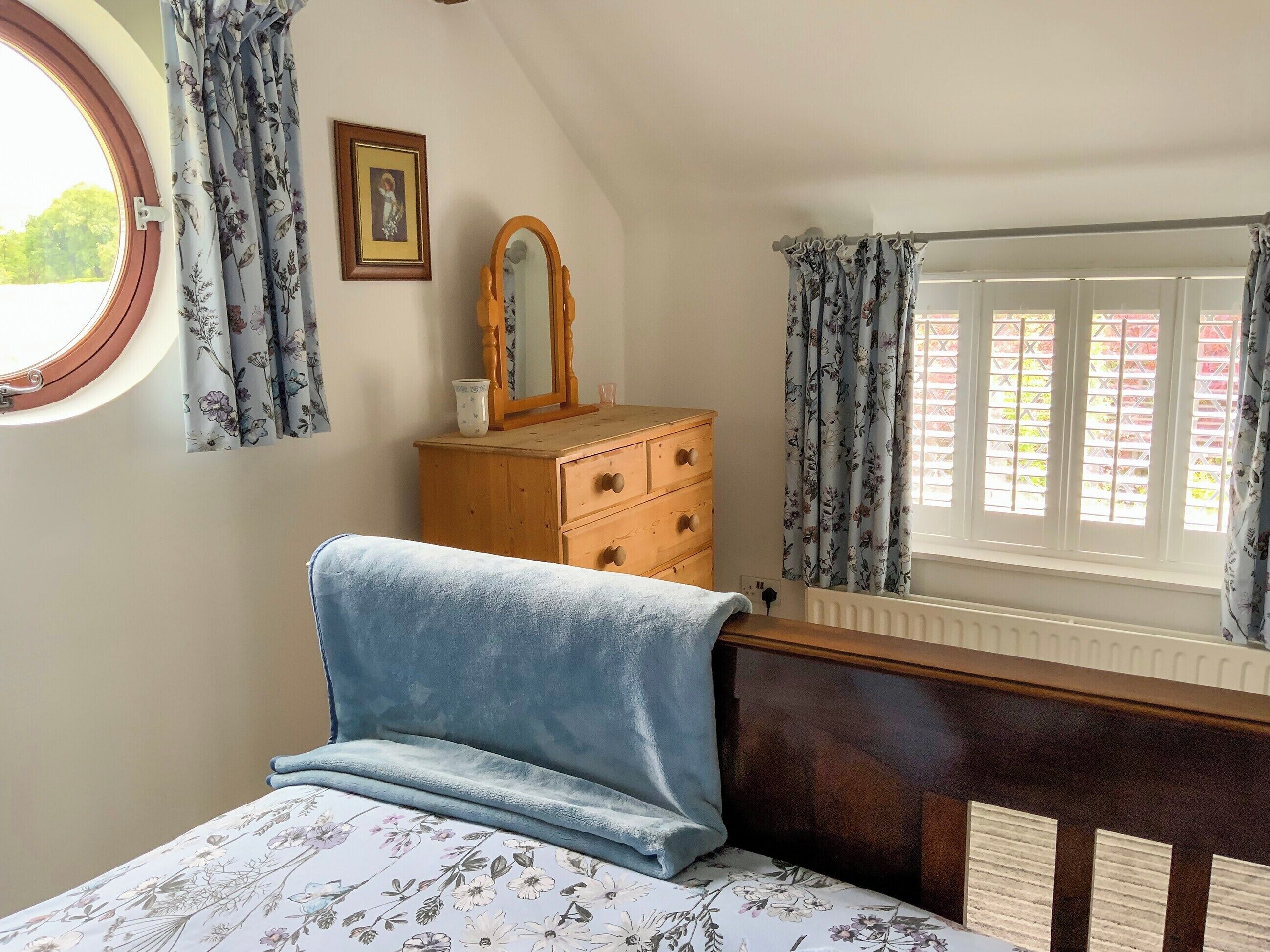 Un dormitorio con cama, cómoda, espejo y ventana con cortinas.