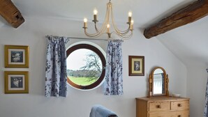 A bedroom with a bed, a dresser, a chandelier, a window with curtains, and framed pictures on the wall. - 1 bedroom accommodation in Betley, near Nantwich (Betley, near Nantwich)