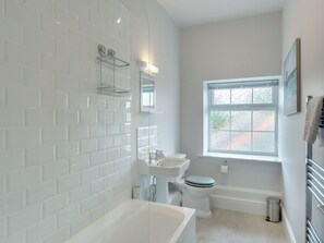 Ein modernes Badezimmer mit weißen Fliesen, einer Badewanne, einer Toilette, einem Waschbecken und einem Fenster mit Milchglas.