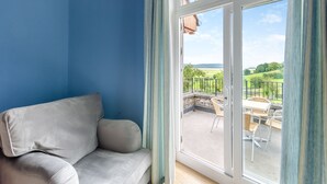 A room with a blue wall, a grey sofa, and a sliding glass door leading to an outdoor patio with a table and chairs. - 2 bedroom accommodation in Meathop, near Grange-over-Sands (Meathop, near Grange-over-Sands)