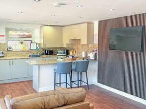 A modern kitchen with granite countertops, a microwave, and a toaster. There are two bar stools and a leather couch in the living area.