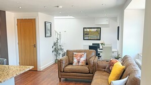 Una sala de estar con un sofá de cuero marrón, una puerta de madera y un comedor con una mesa y sillas blancas.