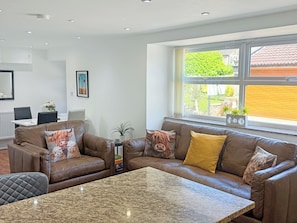 A modern living room with leather sofas, a granite coffee table, and a large window with a view of greenery and a building.