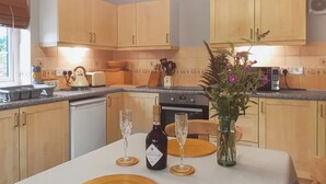 A kitchen with wooden cabinets, a dining table with a white tablecloth, two wine glasses, a bottle of wine, and a vase with flowers. - 1 bedroom accommodation in Mount Hawke (Mount Hawke)