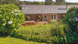 A stone cottage with a tiled roof, surrounded by lush greenery and flowering plants. - 1 bedroom accommodation in Mount Hawke (Mount Hawke)
