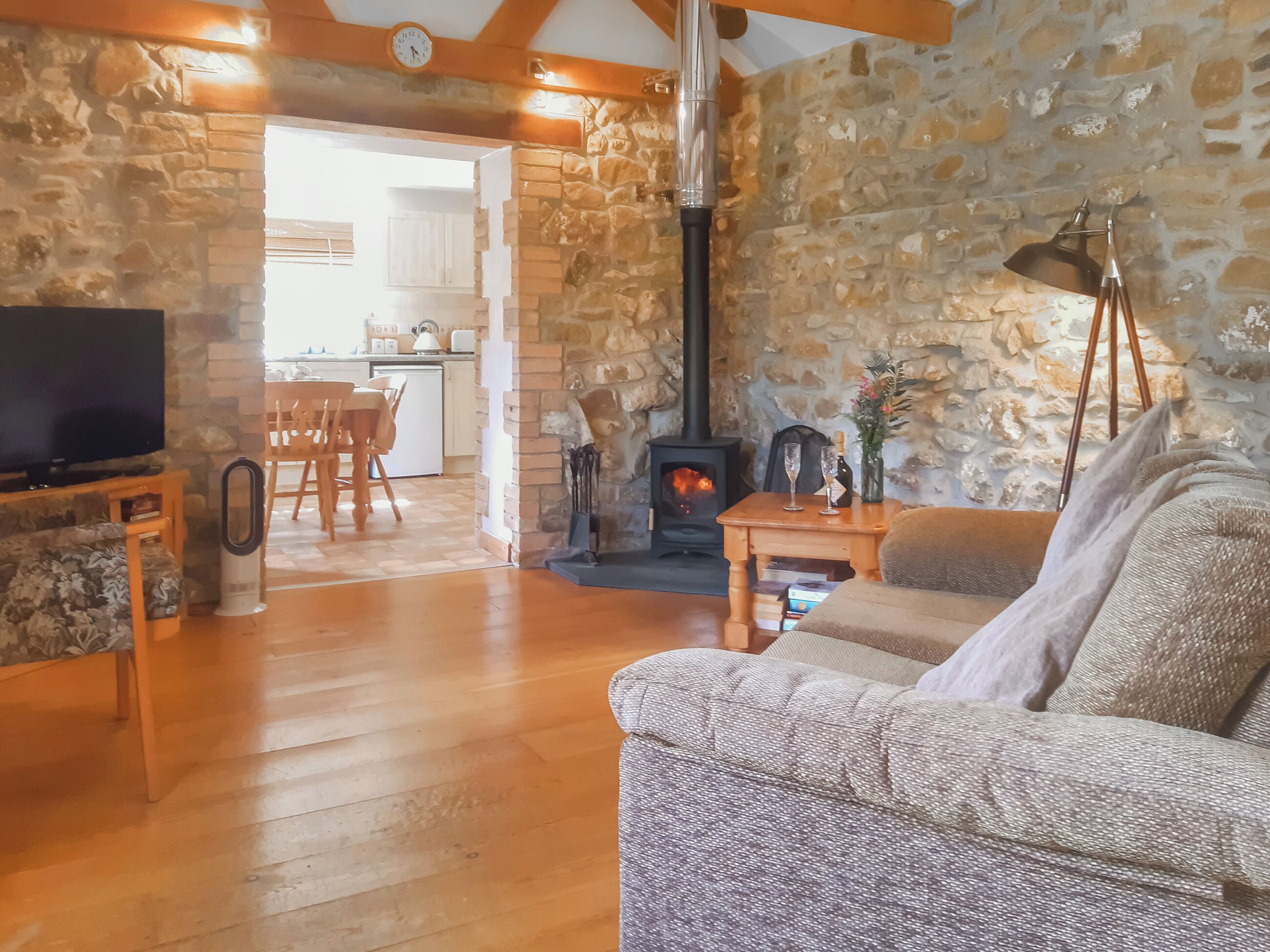 Una sala de estar acogedora con una pared de piedra, una chimenea, un televisor y un comedor visible a través de un arco.