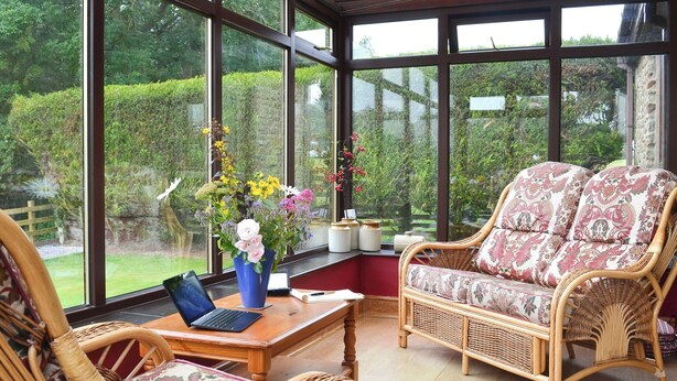 Un invernadero con muebles de mimbre, una computadora portátil y un jarrón de flores.