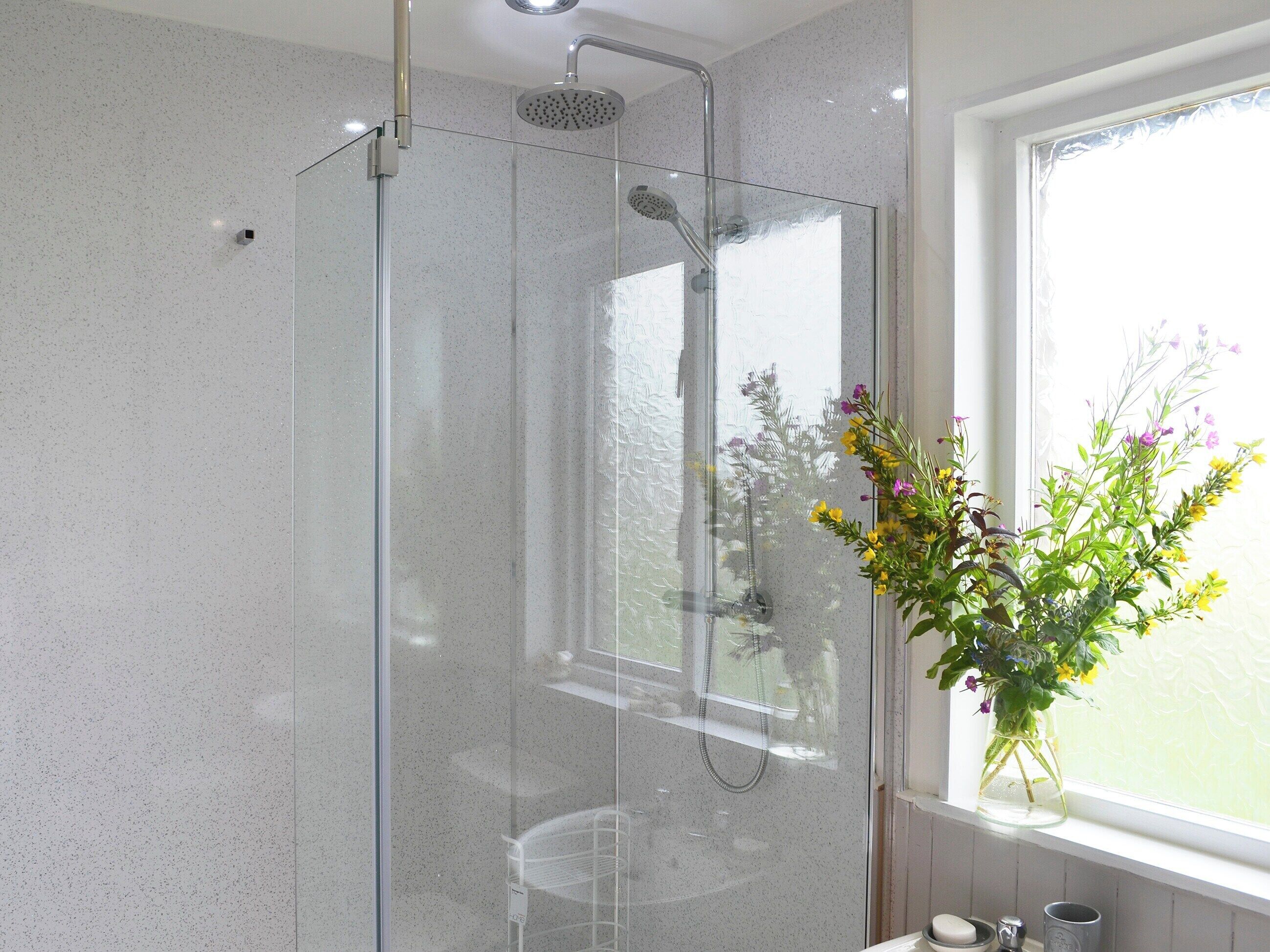 Een douchecabine van glas met een handdouche, een glazen deur en een raam met uitzicht op bloemen.